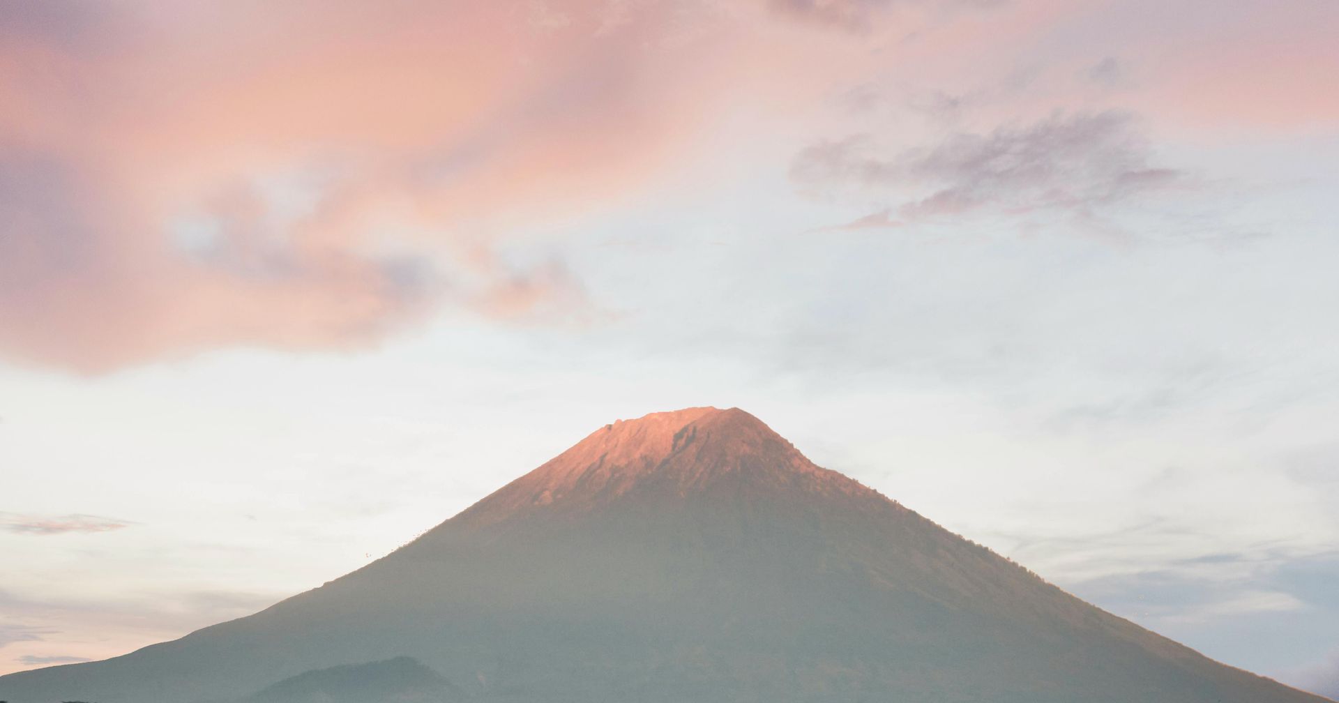 Ein Berg mit einem flachen Gipfel, der von der letzten Abendsonne rosa beleuchtet wird, vor einem Himmel mit vereinzelten Wolken.