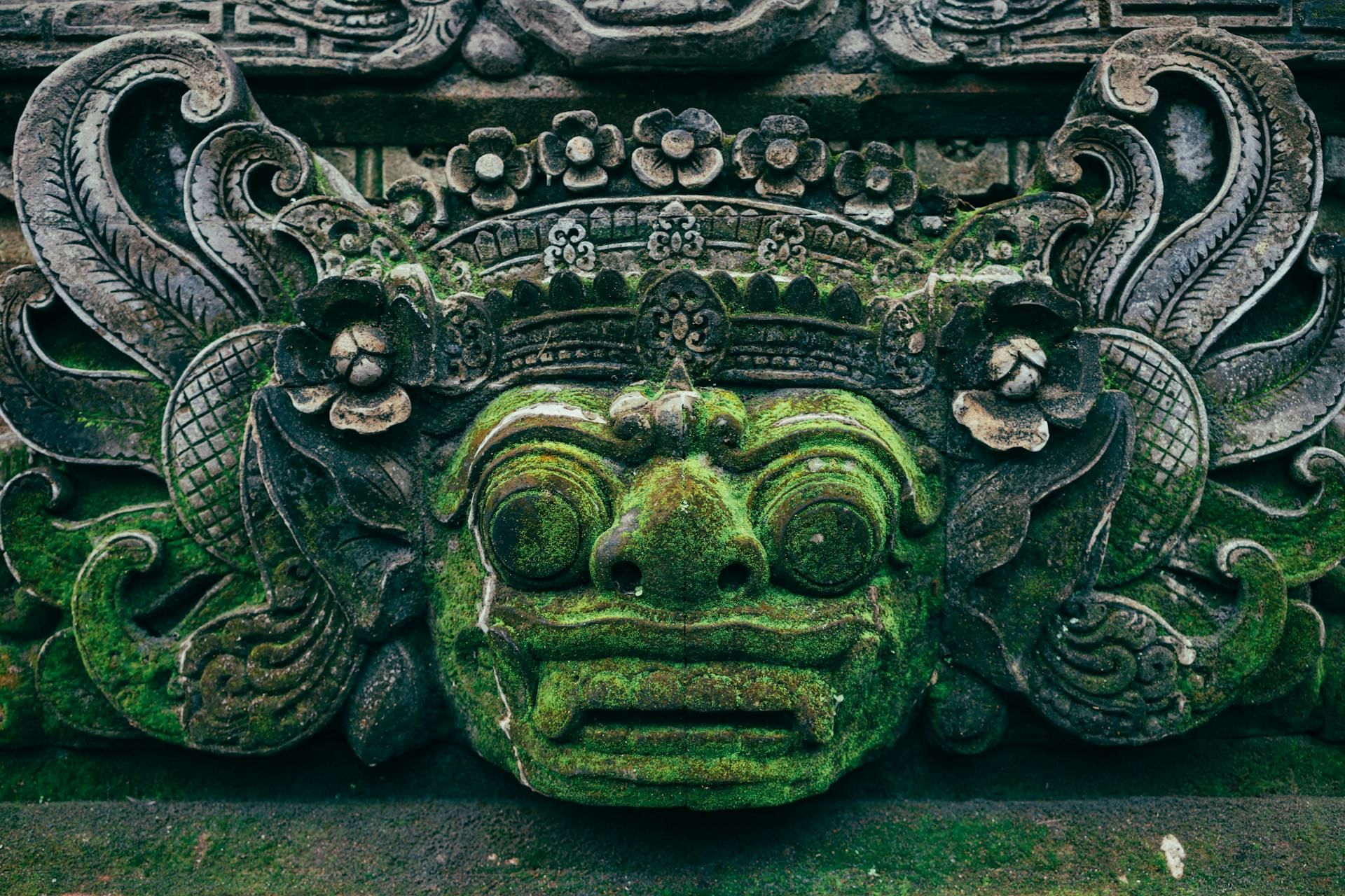 Close-up of an intricately carved stone dragon head covered with moss at a temple in Bali.