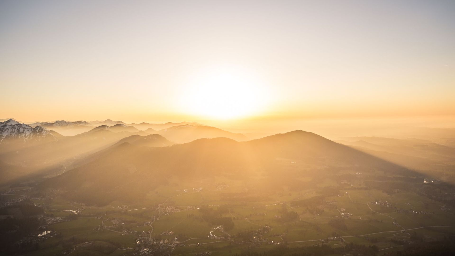Sonnenaufgang über einer berghügeligen Landschaft mit weichem, goldenem Licht und langen Schatten.