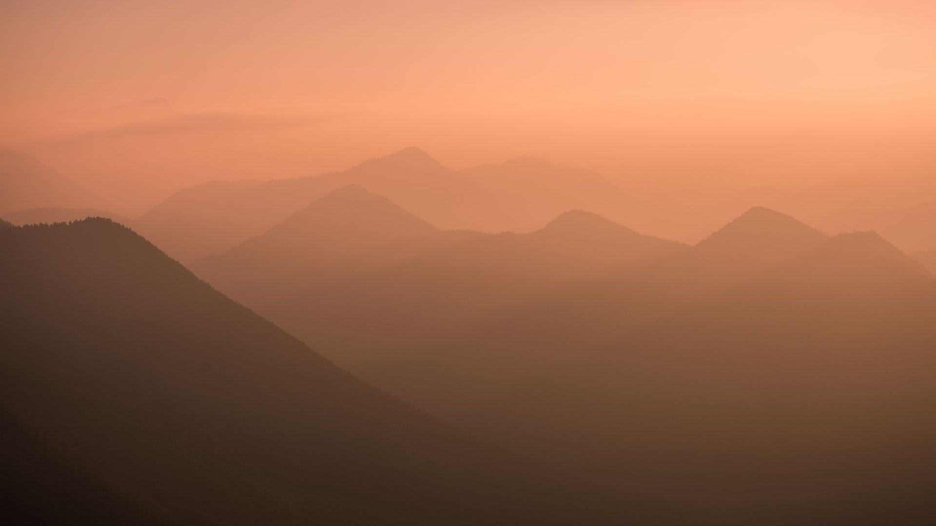 Mehrere Berggipfel in sanften Abstufungen, im warmen Licht eines Sonnenauf- oder -untergangs.