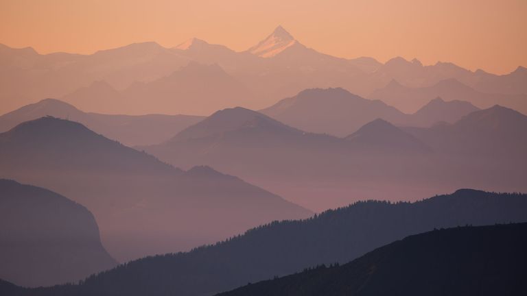 Mehrere Bergketten in unterschiedlichen Lilatönen bei Sonnenuntergang mit dem schneebedeckten Berg Großglockner im Hintergrund.