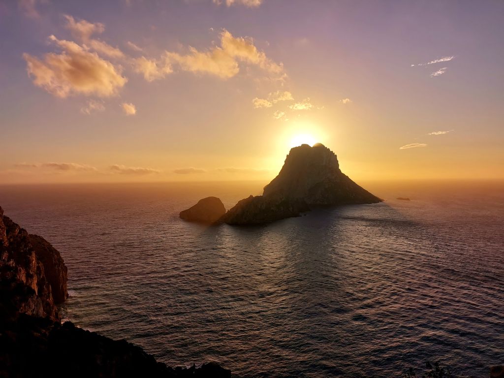 Sonnenuntergang über einer felsigen Insel im Meer mit leicht bewölktem Himmel.