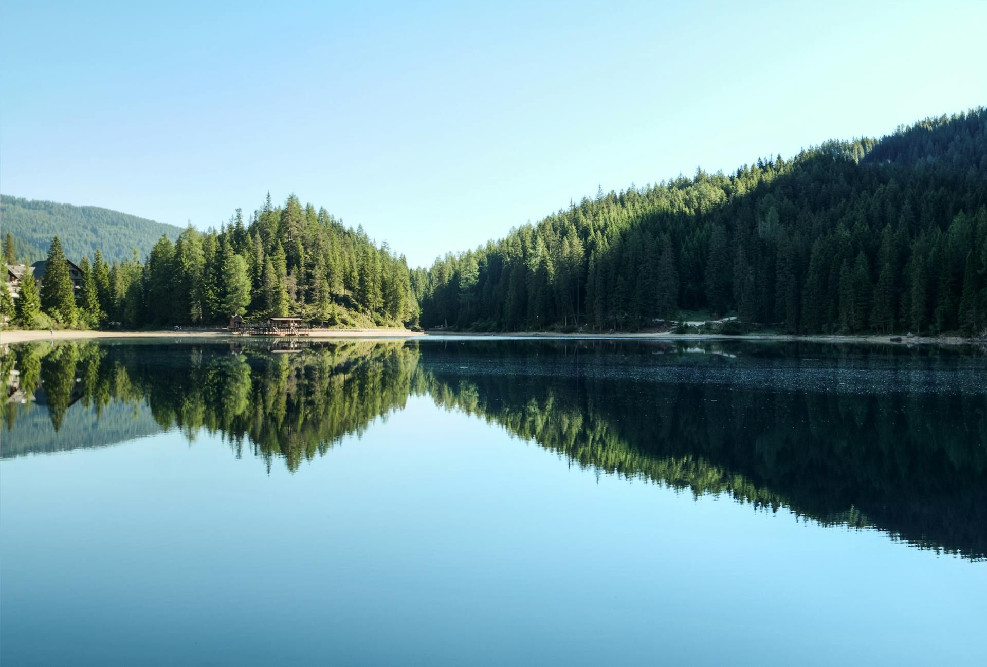 A calm lake reflecting the surrounding forested hills and clear sky in daylight.