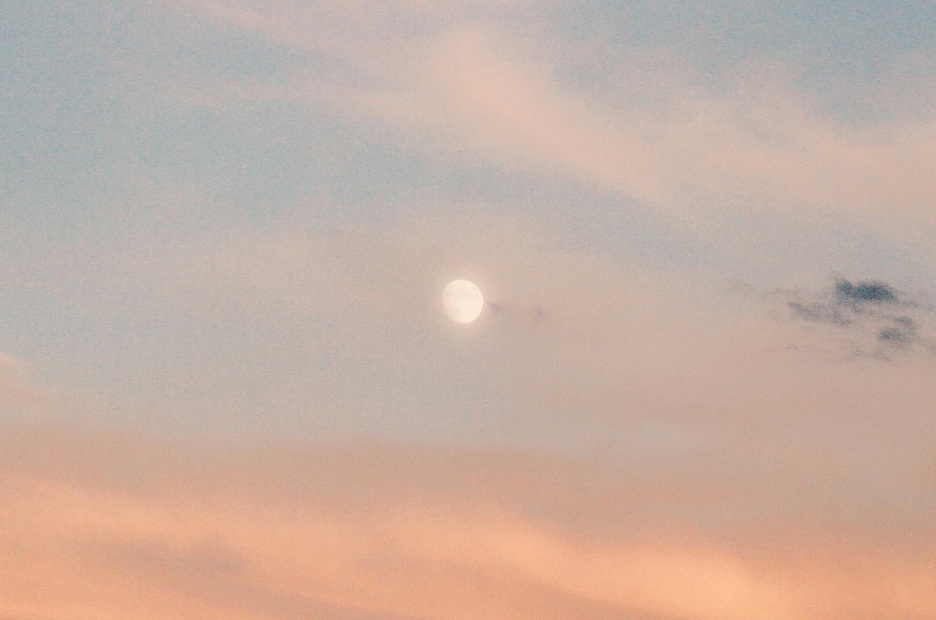 Moon in the sky during a soft sunset with pink and blue clouds.